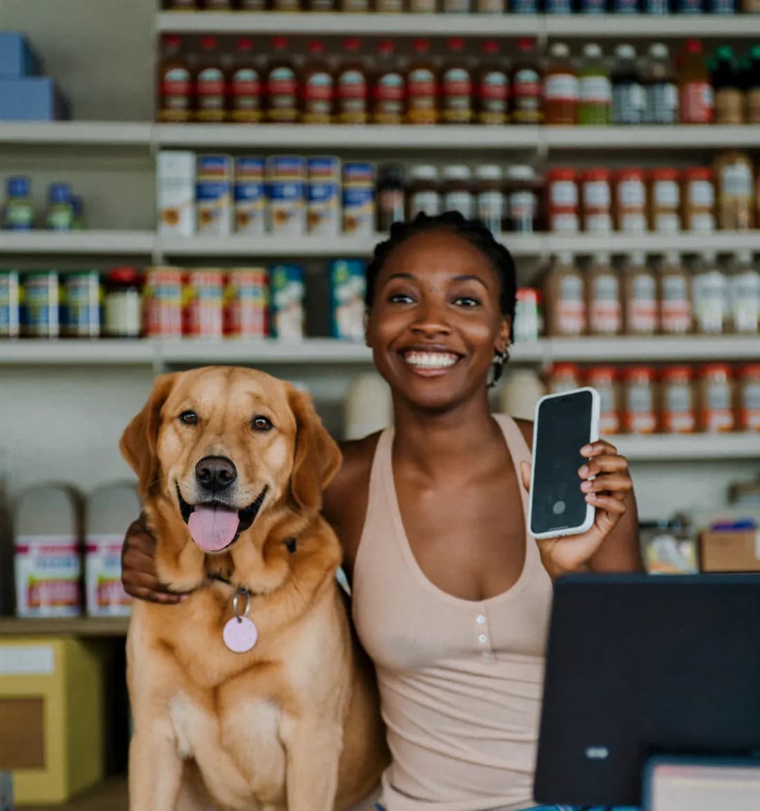 Dona de pet shop sorrindo com o celular na mão e o cachorro ao lado