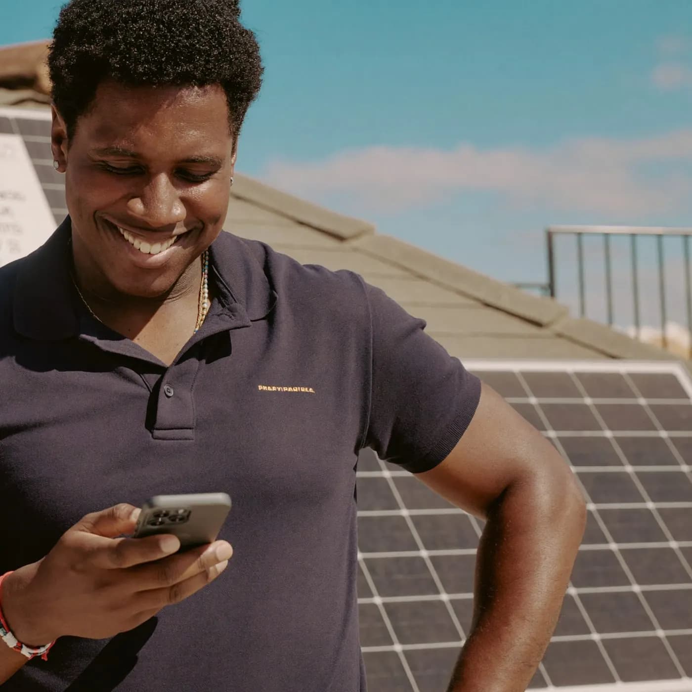 Consultor de energia solar sorrindo ao ler uma mensagem no celular, ao lado de placas solares num telhado