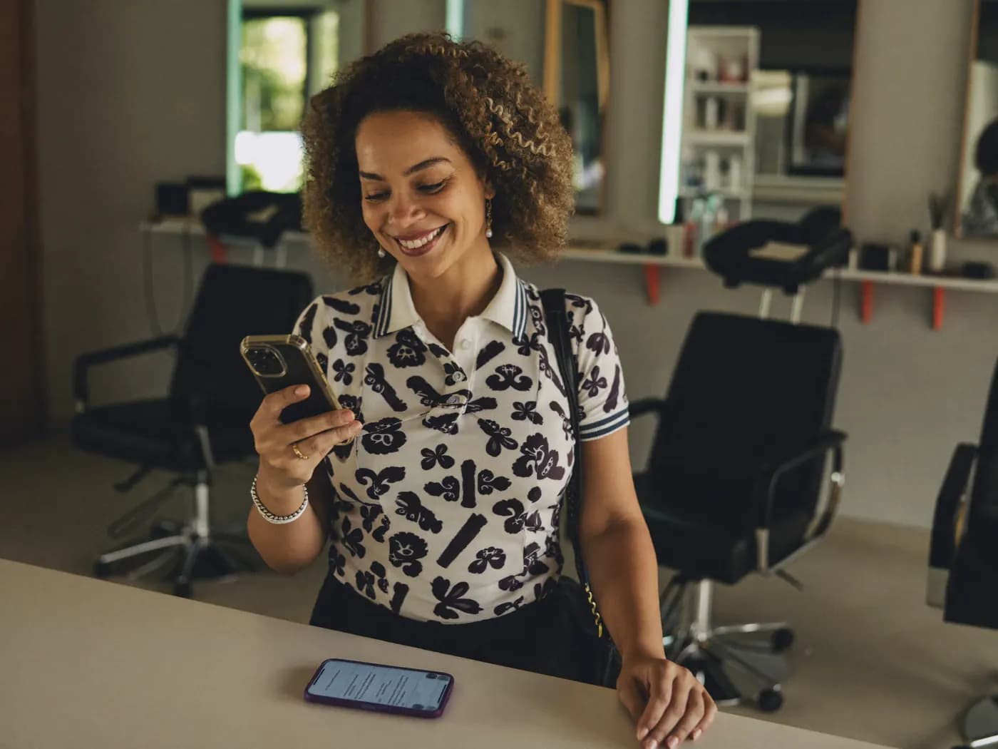 Dona de salão de beleza sorrindo enquanto confere mensagens de clientes no celular
