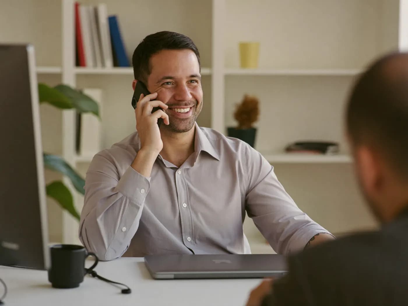 Corretor de seguros sorrindo enquanto conversa com um cliente ao telefone no escritório